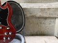 Vintage red cherry electric guitar placed in a black case with a white cement wall background. Popular models.