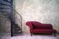 Vintage red leather sofa and retro cast iron spiral staircase on old wall background, copy space for text Royalty Free Stock Photo