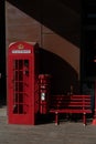 Vintage red phone booth and a wooden bench situated in front of a brick building Royalty Free Stock Photo