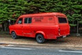 Vintage red van parked alongside a metal chain link fence in a rural outdoor setting. Royalty Free Stock Photo