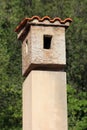 Vintage retro old concrete chimney with red roof tiles on top surrounded with dense trees Royalty Free Stock Photo