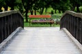 Vintage retro romantic old wooden bridge leading towards wooden public park bench with metal support surrounded with flowers and