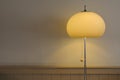 Vintage and retro 70`s style floor lamp standing against a grey wall, with brown wooden paneling. Lights lit.