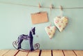 Vintage rocking horse next to fabric hearts and empty card for adding text hanging on the rope on wooden floor