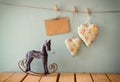Vintage rocking horse next to fabric hearts and empty card for adding text hanging on the rope on wooden floor Royalty Free Stock Photo