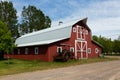 Vintage rusted tractor in front of patrimonial red wooden barn with metal gambrel roof and white trim