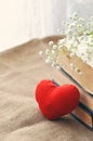 Vintage rustic love card for Valentine`s day-white flowers, yellowed old books and red plush heart on burlap. closeup. tinted.