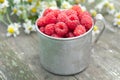 Vintage rustic mug full of raspberries on wooden table and daisy flowers