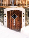 Vintage rustic wooden door of a stone house with winter ornaments and lanters, snowy