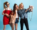 Three young girls in retro 90s fashion style, outfits posing isolated over blue studio background. Concept of eras