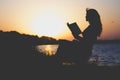 Vintage silhouette of a young beautiful woman at dawn sitting on a folding chair and think about the information which is read Royalty Free Stock Photo