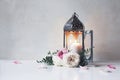 Vintage silver Moroccan, Arabic lantern with glowing candle, green branches, rose flowers and pink petals on white table Royalty Free Stock Photo