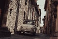 Vintage small Italian car parked in narrow old town street between stone walls. Gubbio, medieval town