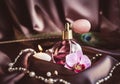 Vintage spray atomizer perfume bottle and pearl jewellery on silky dark pink fabric with peacock feather and candle burning. Royalty Free Stock Photo