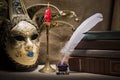 Vintage still life with old books near inkstand, feather, venezian mask and burning red candle in candlestick on canvas background