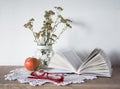 Vintage still life with an open book, glasses, apple and vase with flowers on doily