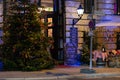 Vintage streetlight on wall. Facade of retro cafe with shiny Christmas decorations and big illuminated Christmas tree Royalty Free Stock Photo