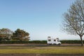 A vintage style camper van with a metal trunk attached to its roof parked on a seafront road with a grassed area in the foreground Royalty Free Stock Photo