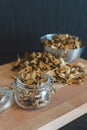 Vintage styled vertical photo of sliced, chopped and dried various mushrooms in preserving glass and silver bowl standing on wood