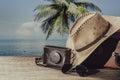 Vintage suitcase, sun hat, photo camera and sunglasses on wooden deck with sea water, coconut palm tree and blue sky background on Royalty Free Stock Photo