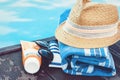 Vintage summer wicker straw beach hat, sun glasses, tube of sunscreen cream, blue towel, near swimming pool, tropical background Royalty Free Stock Photo