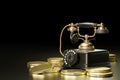 Vintage telephone set on top of stacked gold coins in a dark black background. Royalty Free Stock Photo