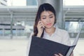 Vintage toned image of attractive young Asian secretary talking on phone and holding document folder on walkway in city Royalty Free Stock Photo