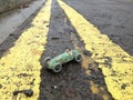 Vintage toy racing car & driver, with worn green paint original patina, between double yellow line on a road.