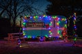 Vintage trailer illuminated with vibrant multicolored lights and lush trees in the background