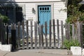 Weathered wooden picket fence borders a pretty white cottage with a blue door. Old Monterey, California.