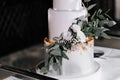 A wedding cake. Sweets. A white cake on a three-tier stand is decorated with eucalyptus, flowers, gold, on a dark background at a