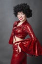 Vintage woman in afro wig and red disco costume on a gray background