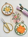 Vintage wooden embroidery hoops, scissors, needle, thread and fabric with floral cross-stitch embroidery on white