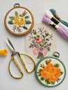 Vintage wooden embroidery hoops, scissors, needle, thread and fabric with floral cross-stitch embroidery on white