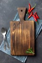 Vintage wooden kitchen board, cutlery and red pepper over napkin on dark stone background. Royalty Free Stock Photo