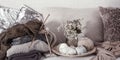 Vintage wooden knitting needles and threads on a cozy sofa with pillows and a vase of flowers Royalty Free Stock Photo