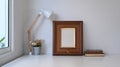 Vintage workspace with empty frame, pot plant, lamp and old book on white table. Royalty Free Stock Photo