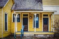 Vintage yellow frame duplex with wood shingle roof and porch with old ornate pillars - grungy