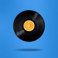 Vinyl record with orange fruit in the centre. Flying in the air. Isolated on blue background. Surrealism levitation concept Royalty Free Stock Photo