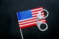 Violation of law, law-breaking concept. Metal handcuffs on American, USA flag on black background top view Royalty Free Stock Photo