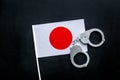 Violation of law, law-breaking concept. Metal handcuffs on Japaniese flag on black background top view