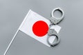 Violation of law, law-breaking concept. Metal handcuffs on Japaniese flag on grey background top view