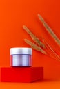 Violet cream glass jar mockup on geometrical podium orange background dry reeds pampas grass. Anti aging skin cosmetics