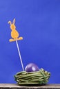A violet easter egg in a green nest, an easter rabbit on the top of rod. Royalty Free Stock Photo