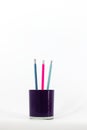 A purple glass desk organizer on a white background holds three pencils with erasers in pink, blue, and navy
