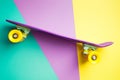 Violet skateboard with yellow wheels on turquoise yellow and purple background. plastic mini cruiser board.
