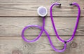 Violet stethoscope on a wooden table. Medical cardiology equipment.