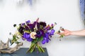 Violet wedding bouquet stands on a table in the interior with the hands of a female florist. Wedding trends