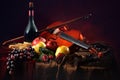 Violin with a bow on a red background next to a bottle of old wine and wet fruit