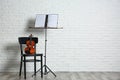 Violin, chair and note stand with music sheets near brick wall. Royalty Free Stock Photo